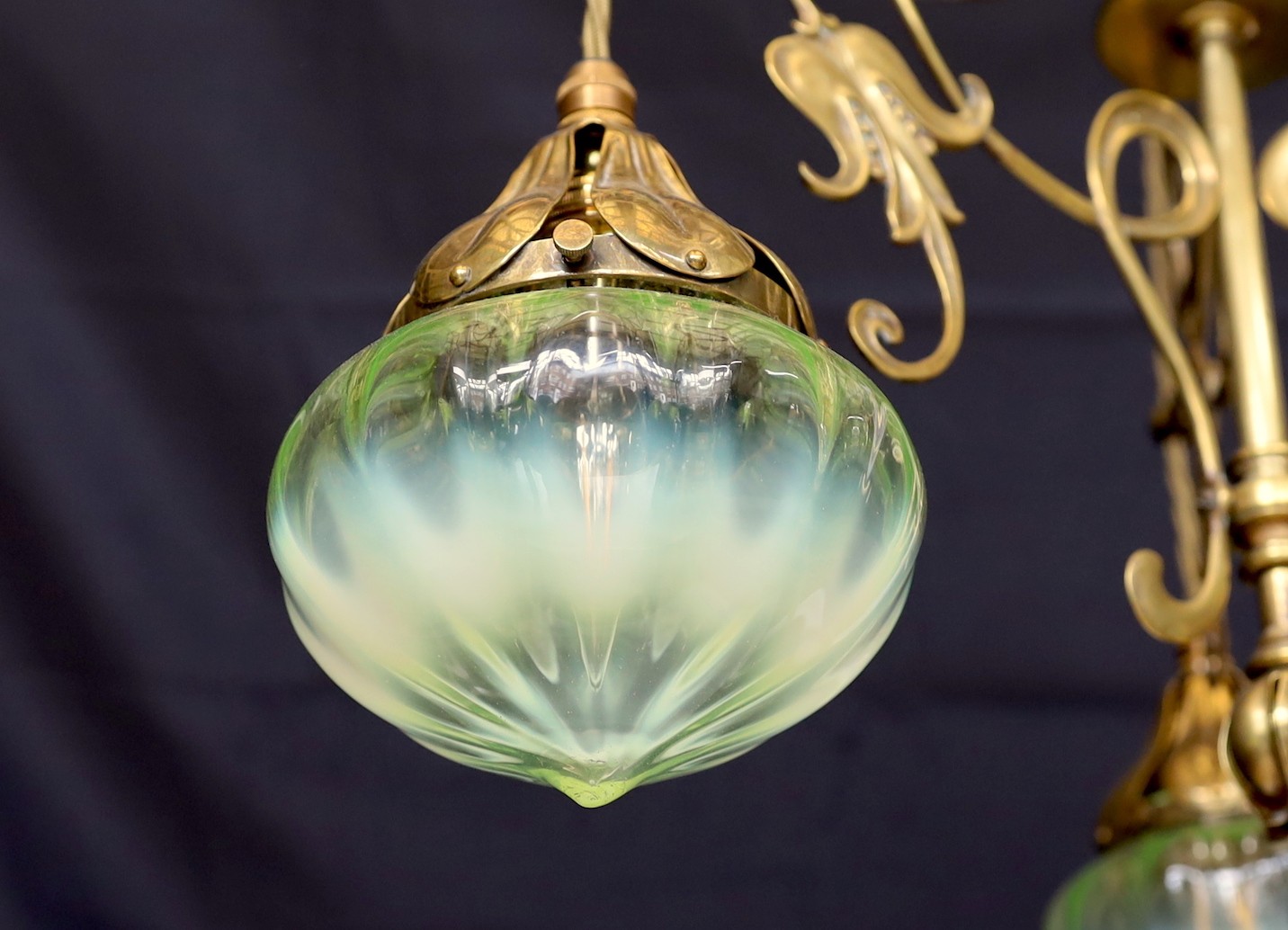 An English Arts & Crafts brass light fitting with scrolling foliate branches and tinted iridescent glass shades, height 68cm. width 46cm
